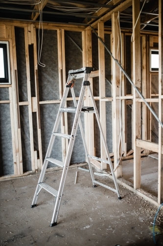 A construction site of a house being built with exposed wires and wooden beams and a ladder - Australian Stock Image
