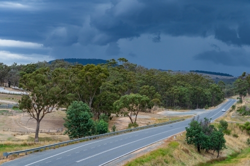 A country road leading past gum trees with dark cloud formations above