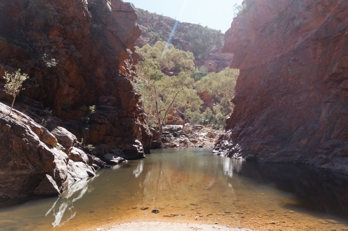 A creek surrounded by rocky cliffs with reddish brown tones - Australian Stock Image