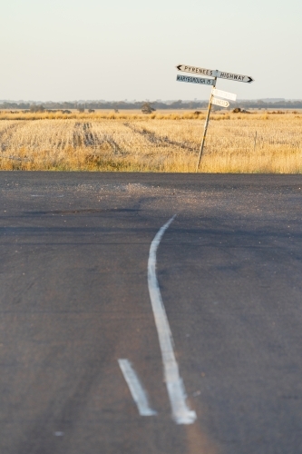 A crooked signpost on a roadside of a rural intersection