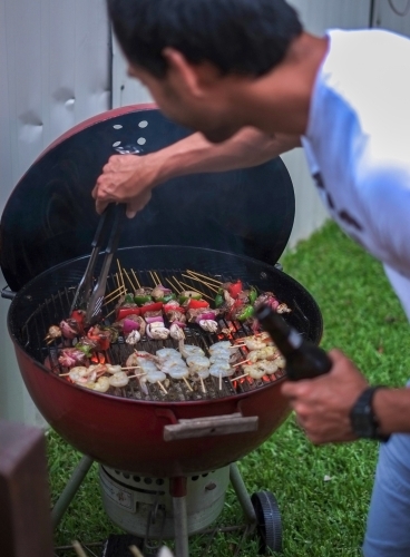 A dad with beer in hand, working the charcoal barbecue - Australian Stock Image