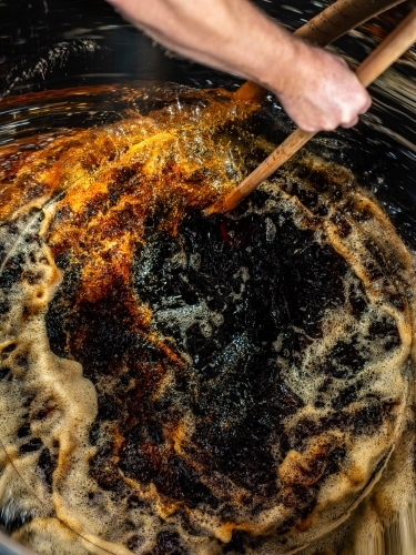 A dark liquid with frothy bubbles and swirls stirred with a wooden paddle - Australian Stock Image