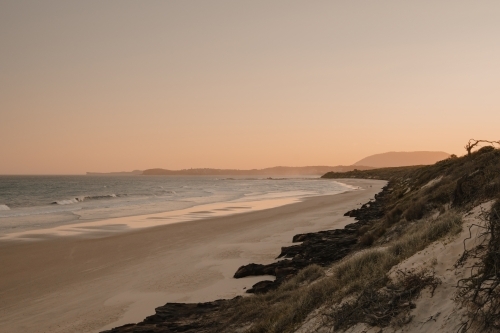 A deserted beach and headland during sunset.