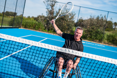 A determined wheelchair tennis player celebrates a successful shot on a bright blue court - Australian Stock Image