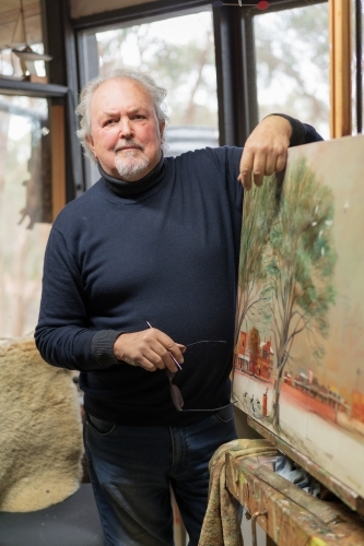 A distinguished male artist leaning on a painted canvas in an art studio