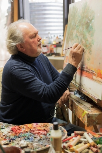 A distinguished male artist painting a canvas in an art studio