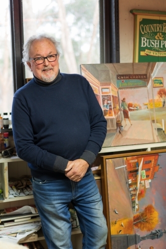 A distinguished male artist standing alongside his paintings in his studio