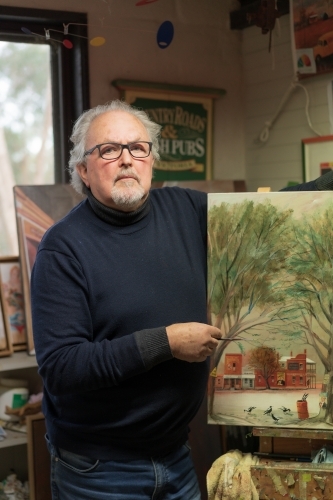 A distinguished male artist standing next to a painted canvas in an art studio