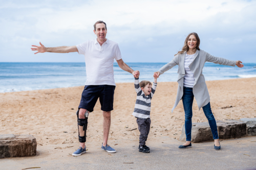 A family at the beach, a man and woman joyfully swinging a boy between them - Australian Stock Image