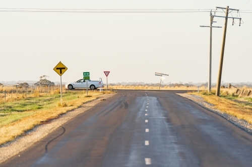 A farm ute passing through a rural T intersection with leaning power poles - Australian Stock Image