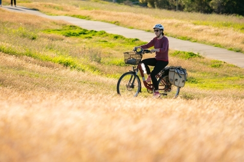 A female cyclist riding along a grassy lined bike path in Brisbane - Australian Stock Image