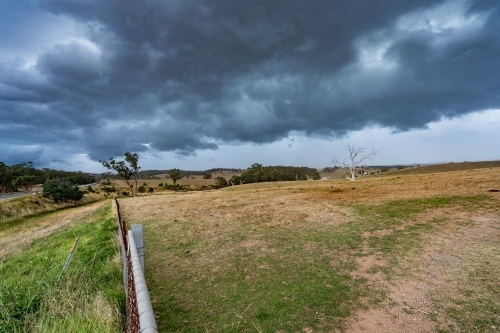 A fence line running over farmland under a dark storm front - Australian Stock Image