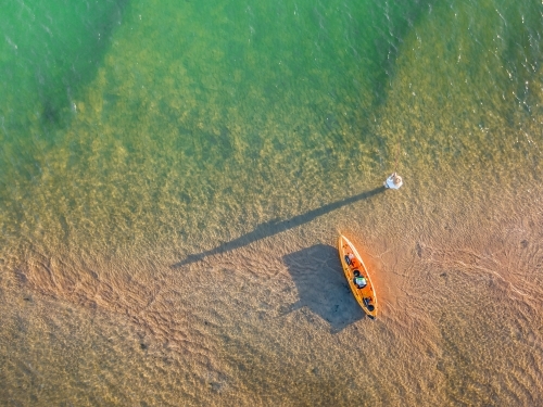 A fishermen alongside a kayak casting long shadows over a river - Australian Stock Image