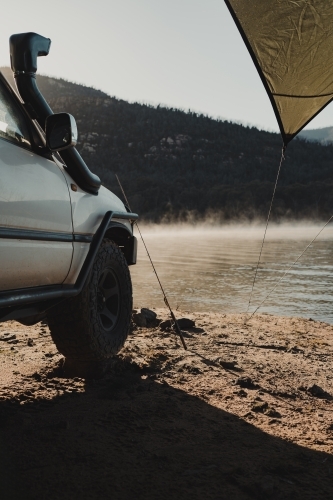 A four wheel drive in front of a lake with fog in the morning light. - Australian Stock Image