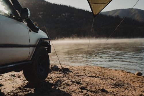 A four wheel drive in front of a lake with fog in the morning light. - Australian Stock Image
