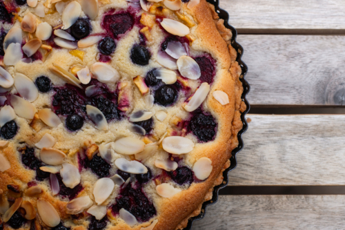 a freshly baked frangepane tart with berries and nuts, on a wooden table - Australian Stock Image