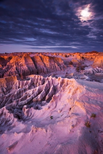 A full moon breaks through cloud above an eroded outback landscape at twilight - Australian Stock Image