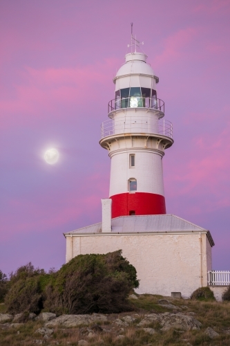 A full moon rising alongside a lighthouse at twilight