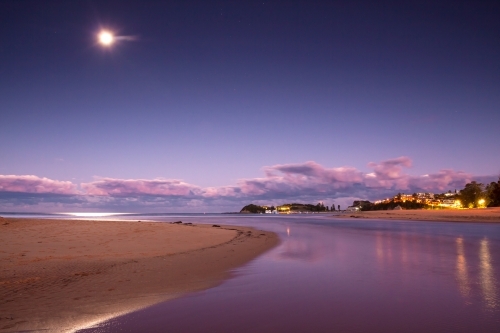 A full moon rising at twilight over a coastal lagoon