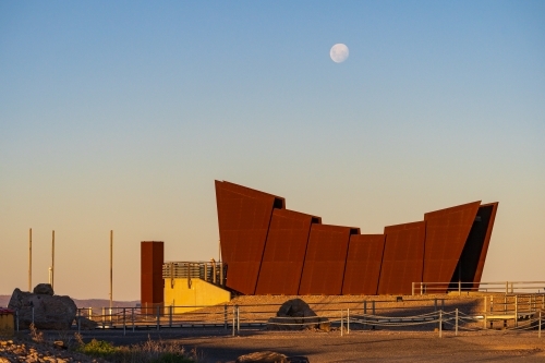 A full moon rising over a big modern metal monument on a hill top