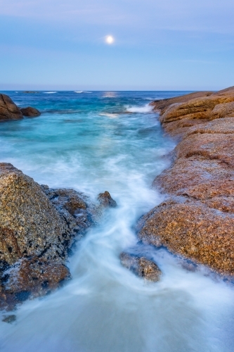 A full moon rising over an inlet along a rocky coastline - Australian Stock Image