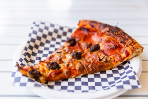 a generous slice of pizza on a paper plate - Australian Stock Image