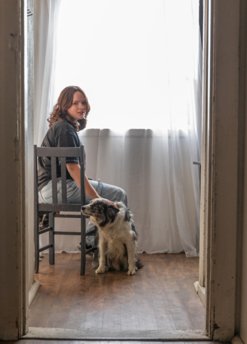 A girl in a doorway sitting on a chair with her dog - Australian Stock Image