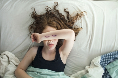 A girl laying in bed pretending to sleep from above - Australian Stock Image