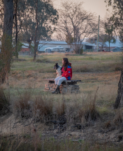 A girl sitting on a bench with her dog in a field - Australian Stock Image