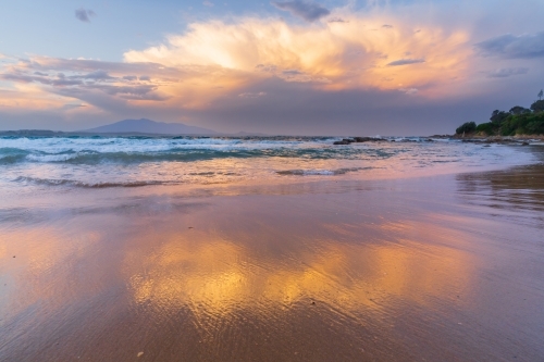A glowing storm cloud reflected on a sandy beach - Australian Stock Image