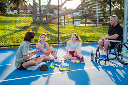 A group of young people engages in tennis practice and talks on a court in the park. - Australian Stock Image