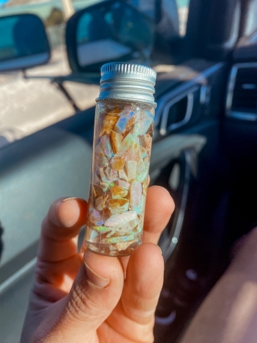 A hand holding a small glass vial of opal shards - Australian Stock Image