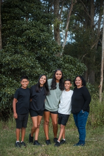 A happy Aboriginal family standing in front of bushland for family portrait - Australian Stock Image