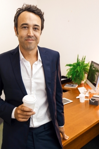 A happy male office worker standing in front of work desk - Australian Stock Image