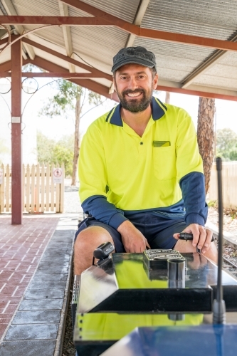 A happy train driver sitting aboard the controls of a miniature train - Australian Stock Image