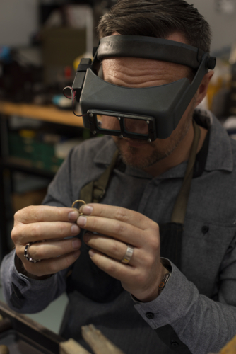 A jeweller wearing goggles and focusing on a ring in his hands - Australian Stock Image