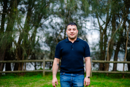 A man in his thirties stands in a tranquil park setting surrounded by trees and water - Australian Stock Image