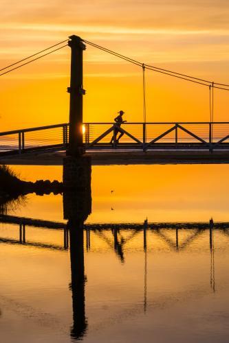 A lady runs across a footbridge at sunrise
