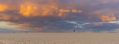 A large colourful cloud bank over a wide sandy beach at dusk - Australian Stock Image