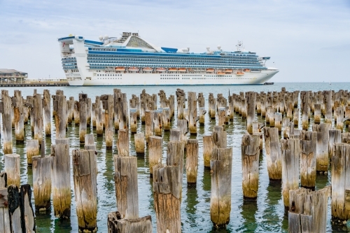 A large cruise docked near many rows of old weathered jetty pylons - Australian Stock Image