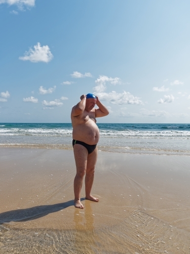 A large man putting on a swimming cap standing on an empty beach
