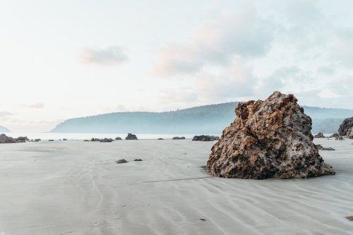 A large, textured rock formation stands on a sandy beach. - Australian Stock Image