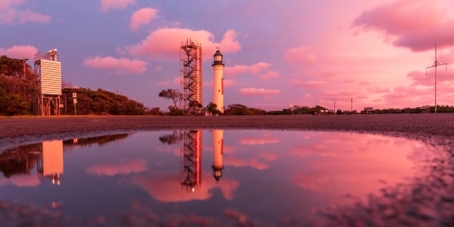 A lighthouse and its reflection against a colourful sunset sky
