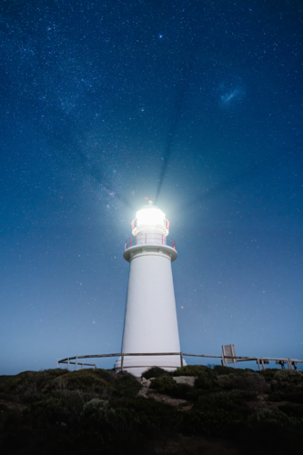 A lighthouse stands illuminated beneath a vast, star‑filled sky - Australian Stock Image