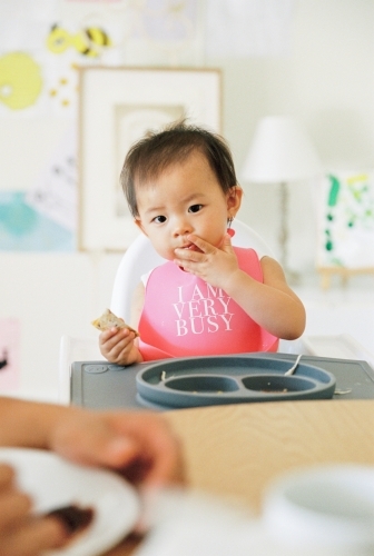 A little girl toddler eating a healthy meal on a highchair - Australian Stock Image