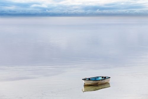 A lone dinghy tied up on still water - Australian Stock Image