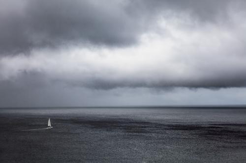 A lone yacht sailing the ocean under stormy grey skies