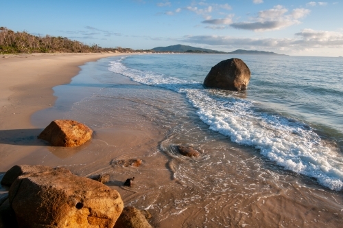 A long beach with boulders in the foreground taken around sunrise