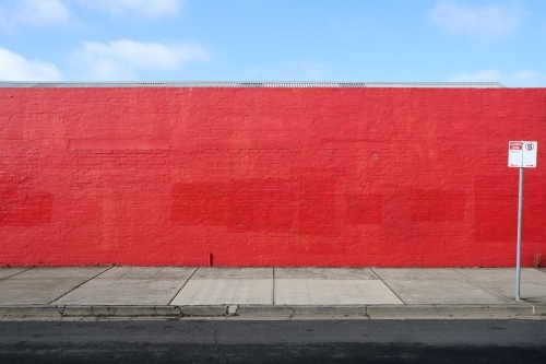 A long red wall with a street sign in front of it