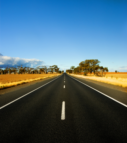 A long, straight country road stretches toward the horizon beneath a vivid blue sky - Australian Stock Image